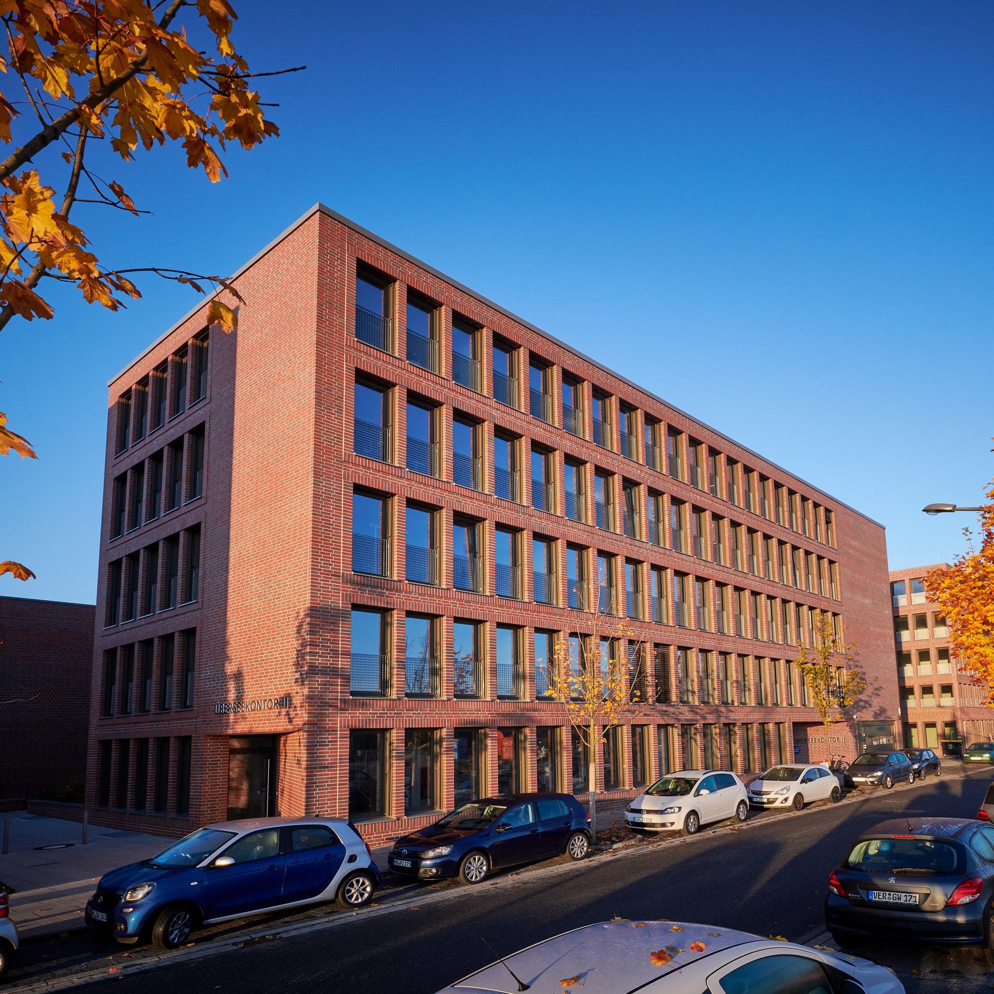 Modernes Backsteingebäude an Straße mit geparkten Autos bei Sonne