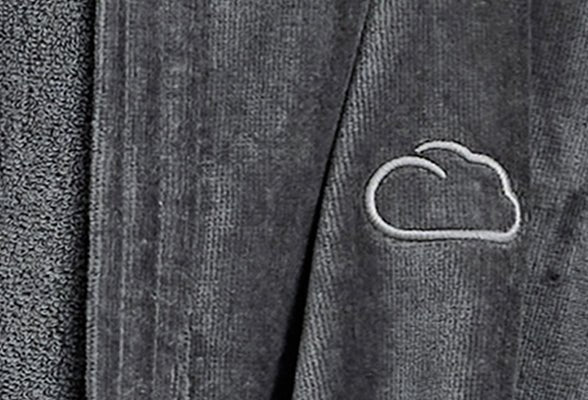 Dunkelgrauer Bademantel mit eingestickter Wolke neben Handtuch aus Frottee