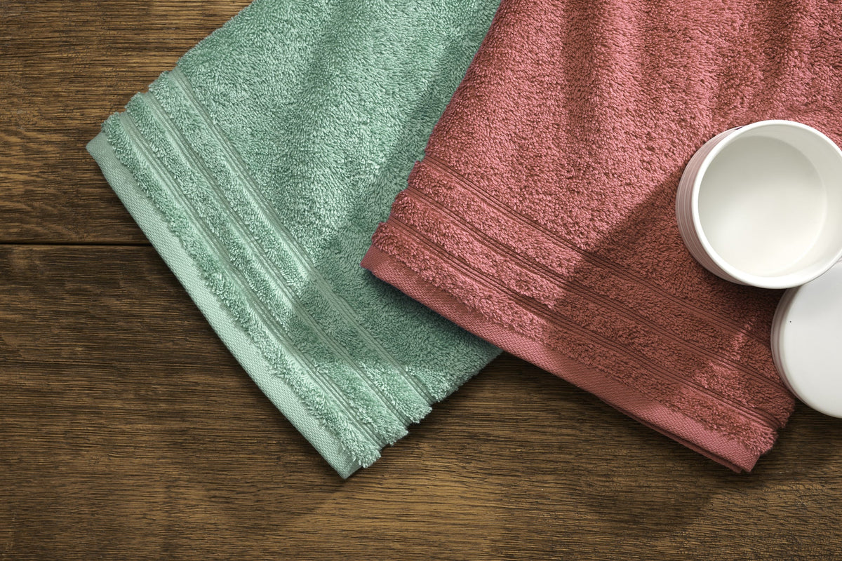 Mintgrünes und roséfarbenes Handtuch neben zwei weißen Cremedosen