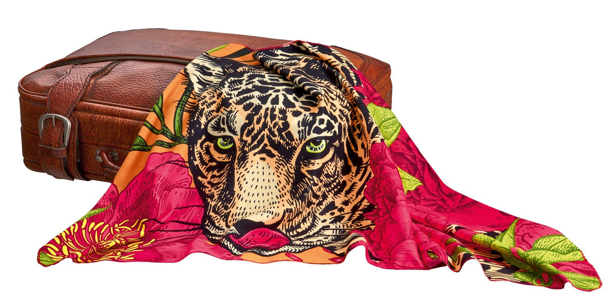 Buntes Badetuch mit Leopardenmotiv, ausgebreitet auf Lederkoffer liegt