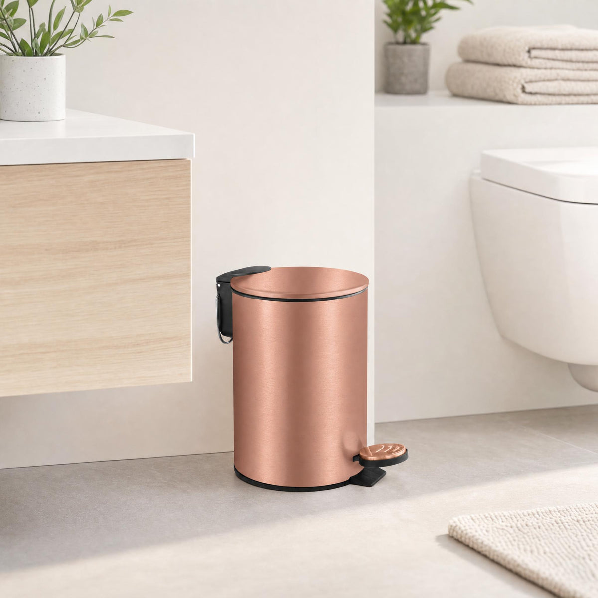 Roségoldfarbener Treteimer in hellem Bad neben Waschtisch und WC.