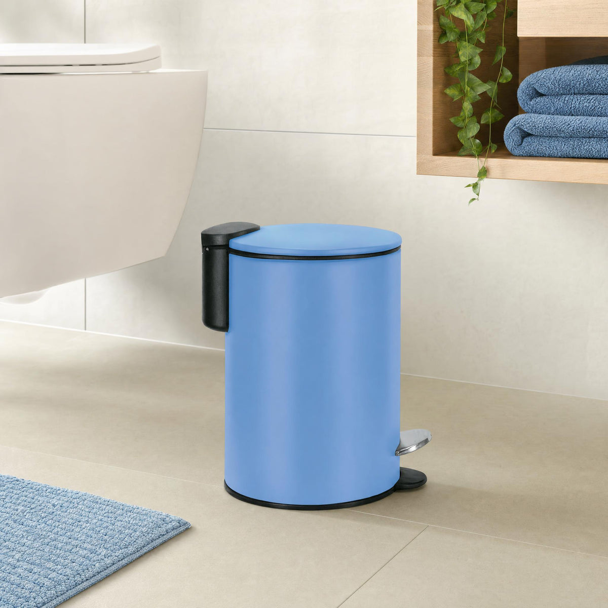 Blauer Treteimer im modernen Bad neben Toilette und Regal mit Handtüchern.