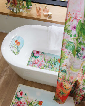 Badewanne mit floralem Vorhang, Badematte und Kissen in Pastellfarben.