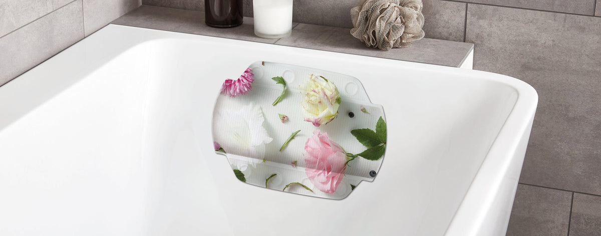 Weiße Badewanne mit floralem Nackenkissen und Deko im Hintergrund