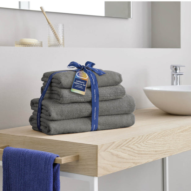 Graues Handtuch-Set mit Schleife auf Holzablage neben Waschbecken