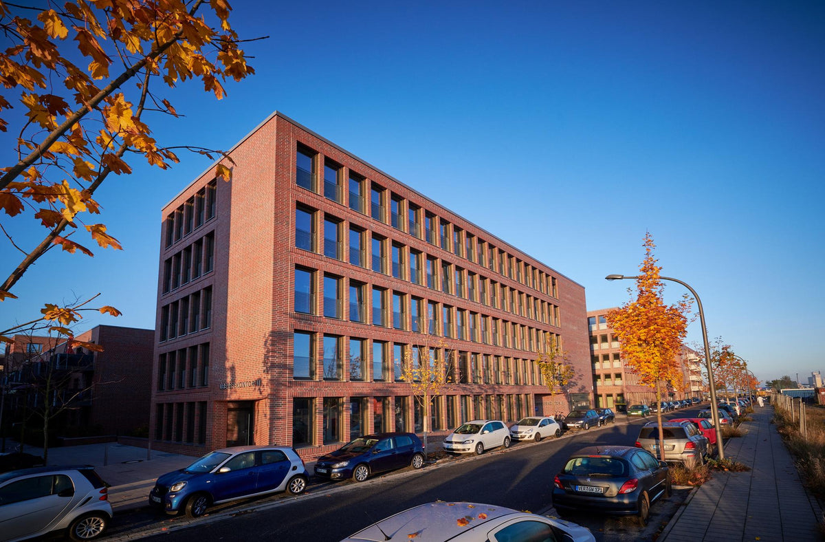 Moderner Backstein-Bürokomplex an Straße mit parkenden Autos im Sonnenlicht