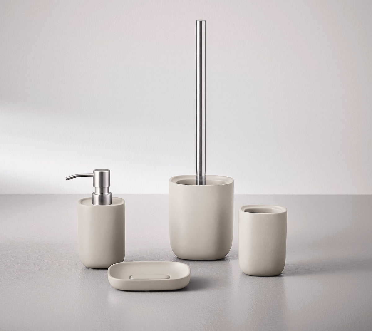Beiges Badset mit Seifenspender, Becher, Schale und WC-Bürste auf Grau