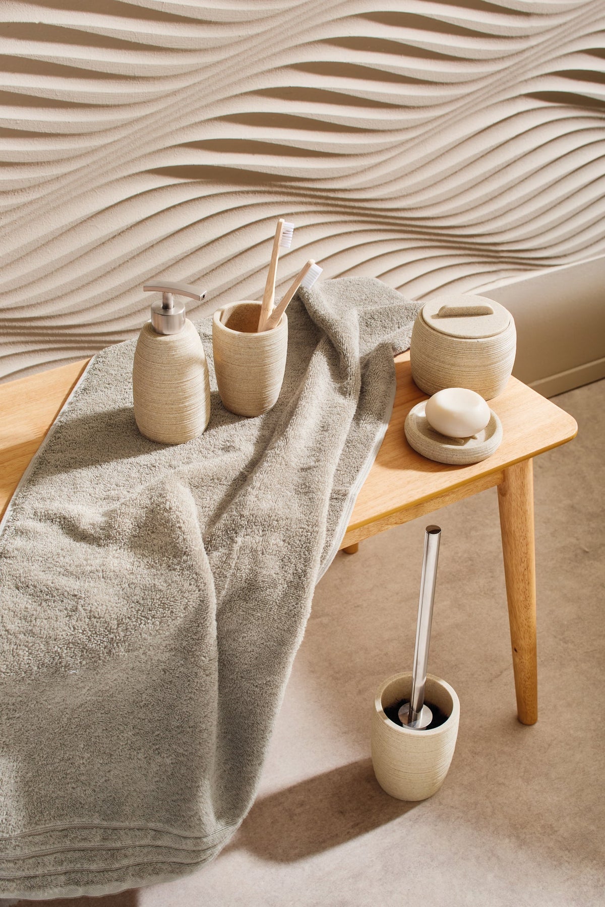 Holzbank mit Handtuch und beigen Badaccessoires vor Wellenfliesen