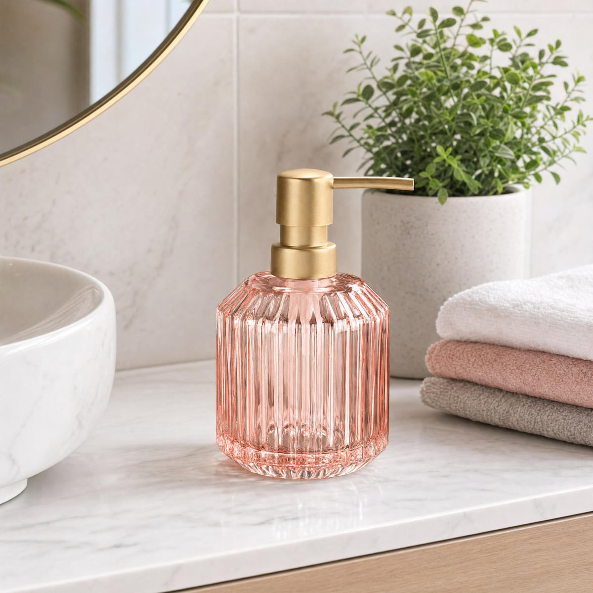 Rosa Seifenspender aus Glas mit goldfarbenem Pumpenkopf in hellem Bad.