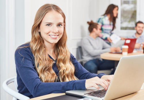 Junge Frau mit Laptop sitzt lächelnd an Schreibtisch im hellen Büro