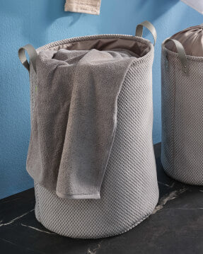 Grauer Wäschekorb mit Handtuch vor blauer Wand im Badezimmer.