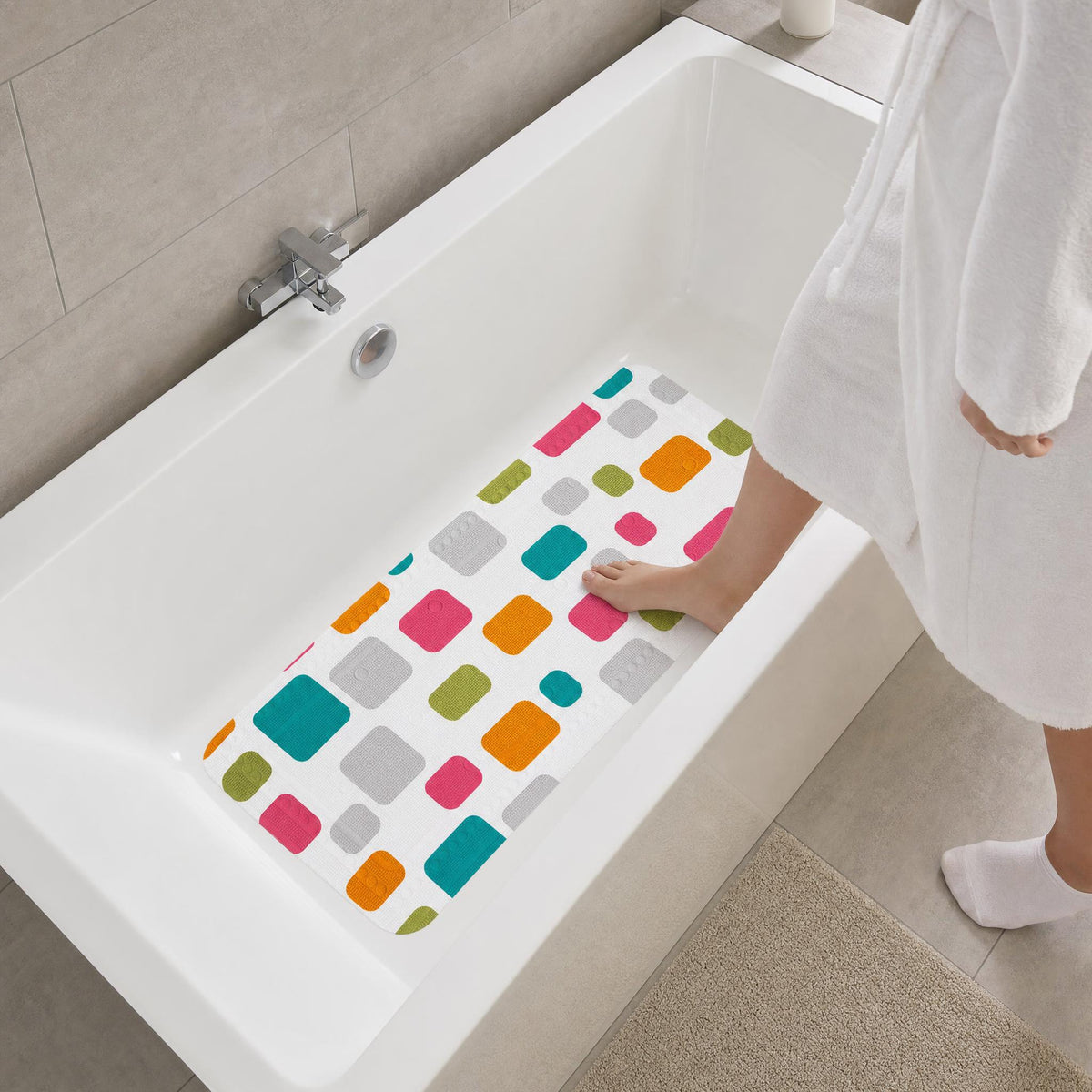 Person im Bademantel steigt in Badewanne mit bunter Antirutschmatte.
