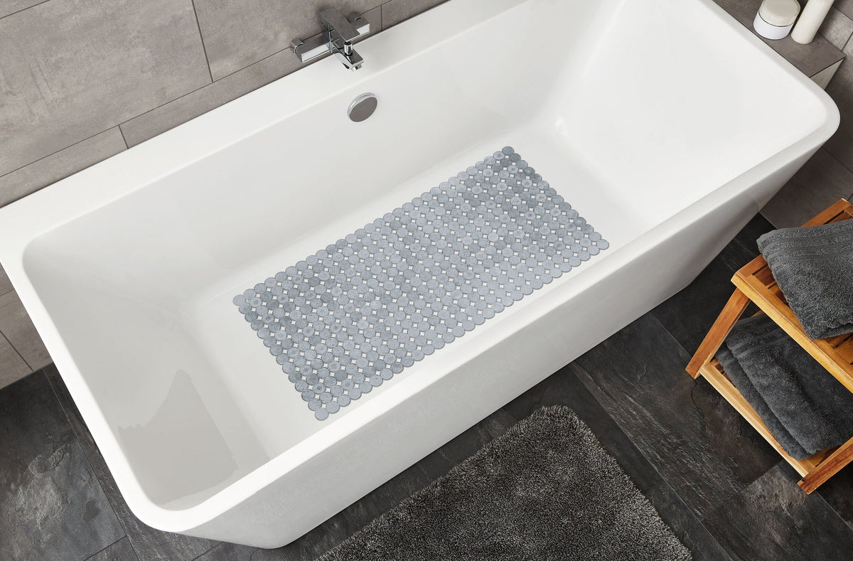 Weiße Badewanne mit grauer rutschfester Badematte und grauem Teppich