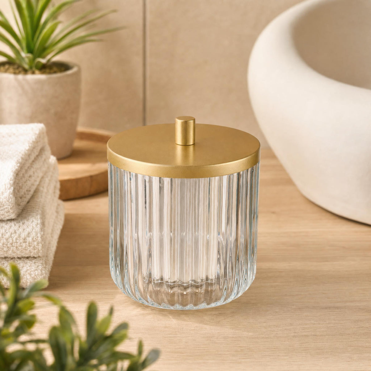 Geriffeltes Glasgefäß mit Golddeckel auf Holzablage im Badezimmer.