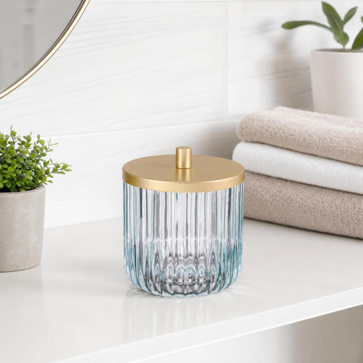 Geriffelte Glasdose mit goldfarbenem Deckel auf weißer Ablage im Badezimmer.