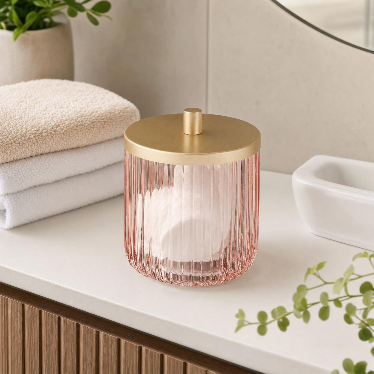 Rosa Glasdose mit goldfarbenem Deckel auf modernem Badwaschtisch.