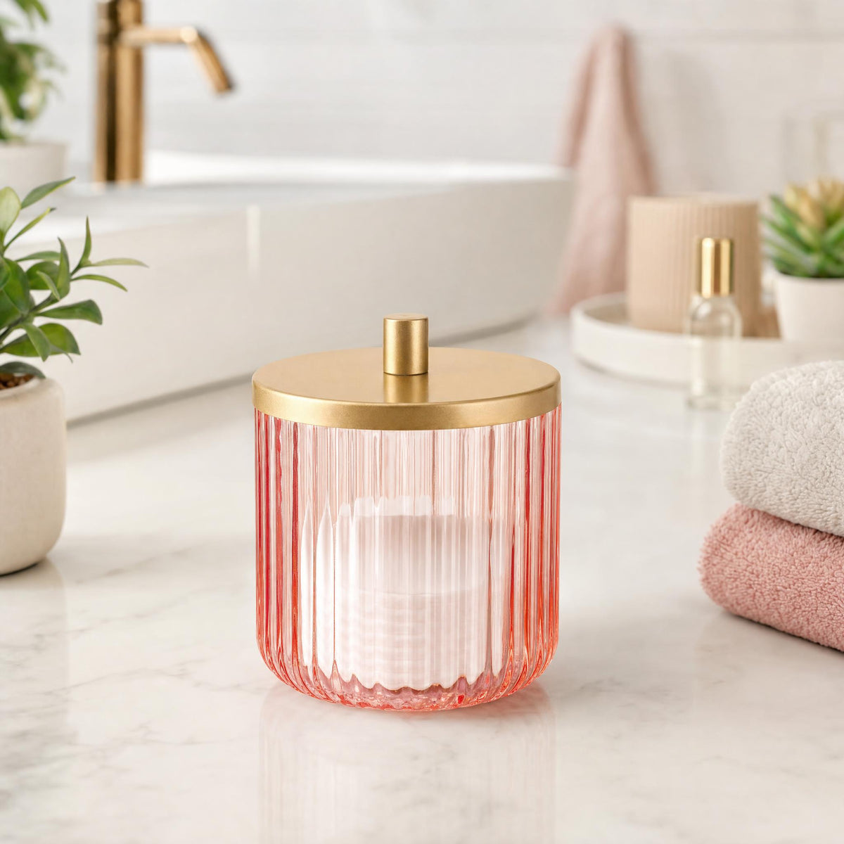 Rosa Glasdose mit goldfarbenem Deckel auf Waschtisch im hellen Badezimmer.