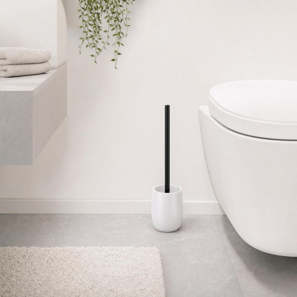 Weiße WC-Bürste mit schwarzem Griff steht neben der Toilette.