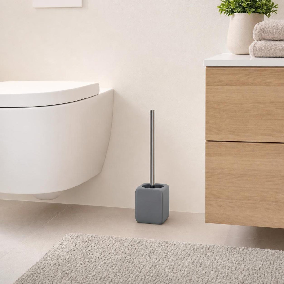 Graue WC-Bürste steht neben Toilette und Holzwaschtisch im Bad.