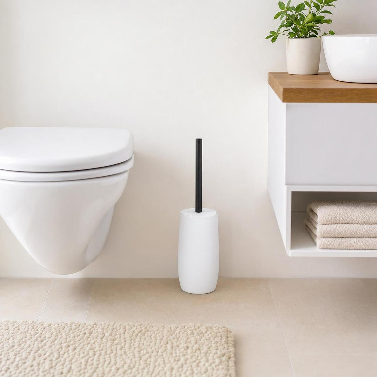 Weiße WC-Bürste mit schwarzem Griff steht neben der Toilette im Bad.