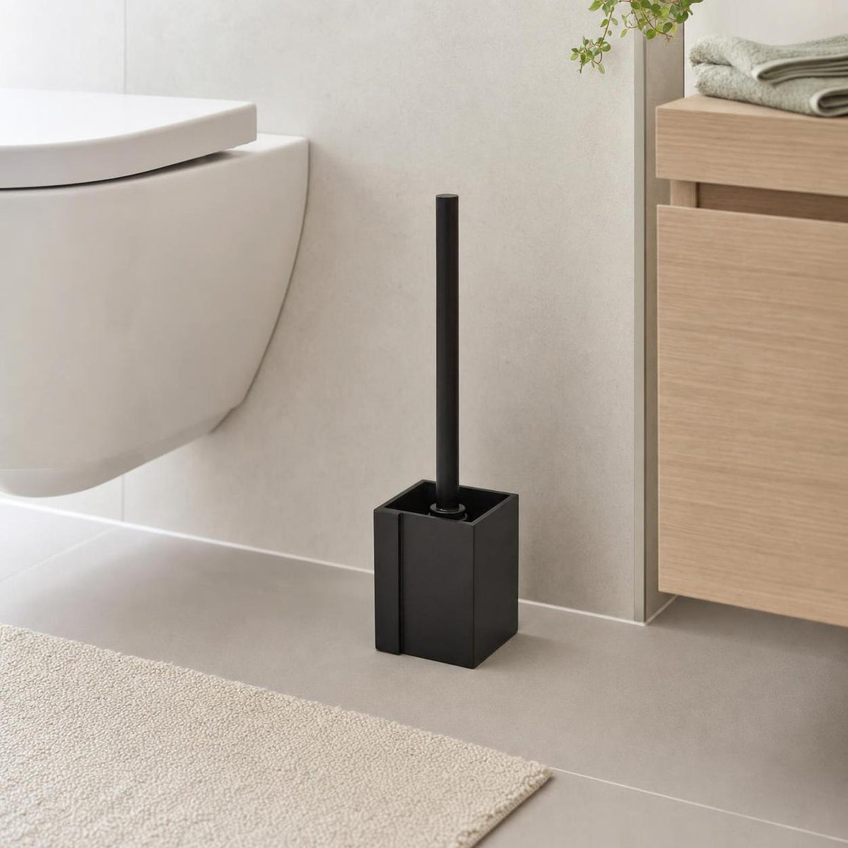 Schwarze WC-Bürste steht neben Toilette und Holzschrank im Bad.