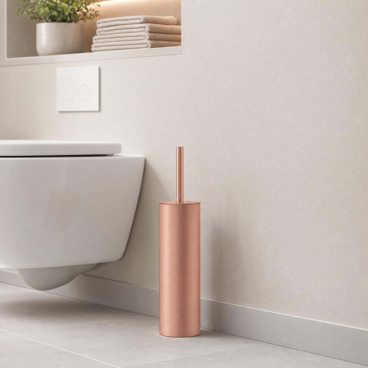 Roségoldfarbene WC-Bürste neben wandhängendem WC in modernem Bad.