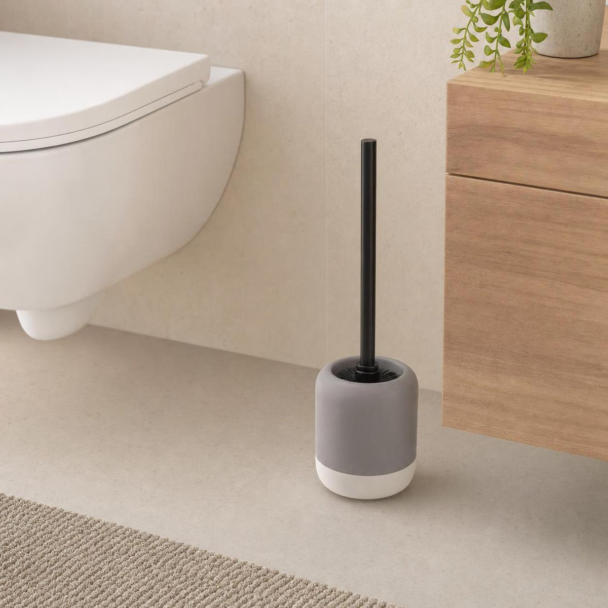 Graue WC-Bürste mit schwarzem Griff steht neben Toilette und Holzschrank.