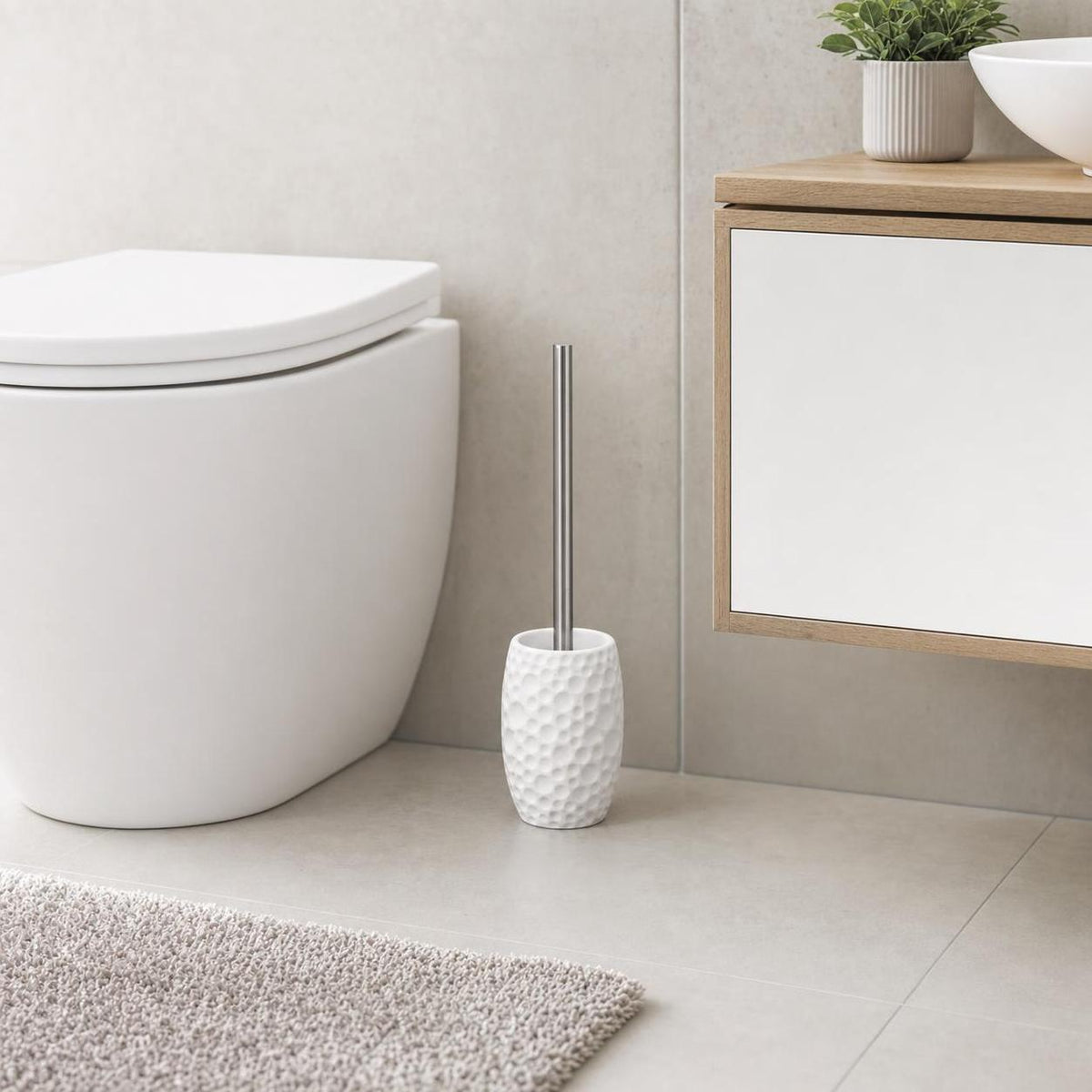 Weiße WC-Bürste mit strukturierter Halterung steht neben der Toilette.