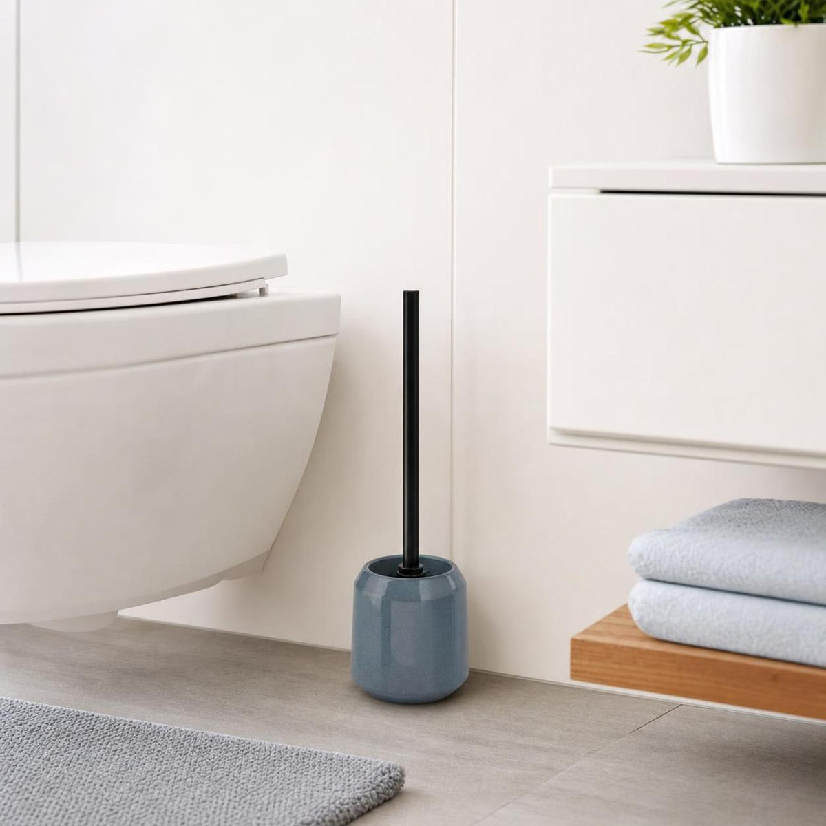 Eine blaue Toilettenbürste steht neben der Toilette im hellen Bad.