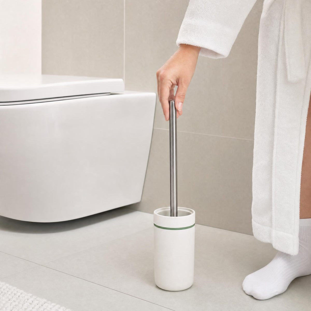 Person im Bademantel hält Toilettenbürste neben modernem WC im Bad.