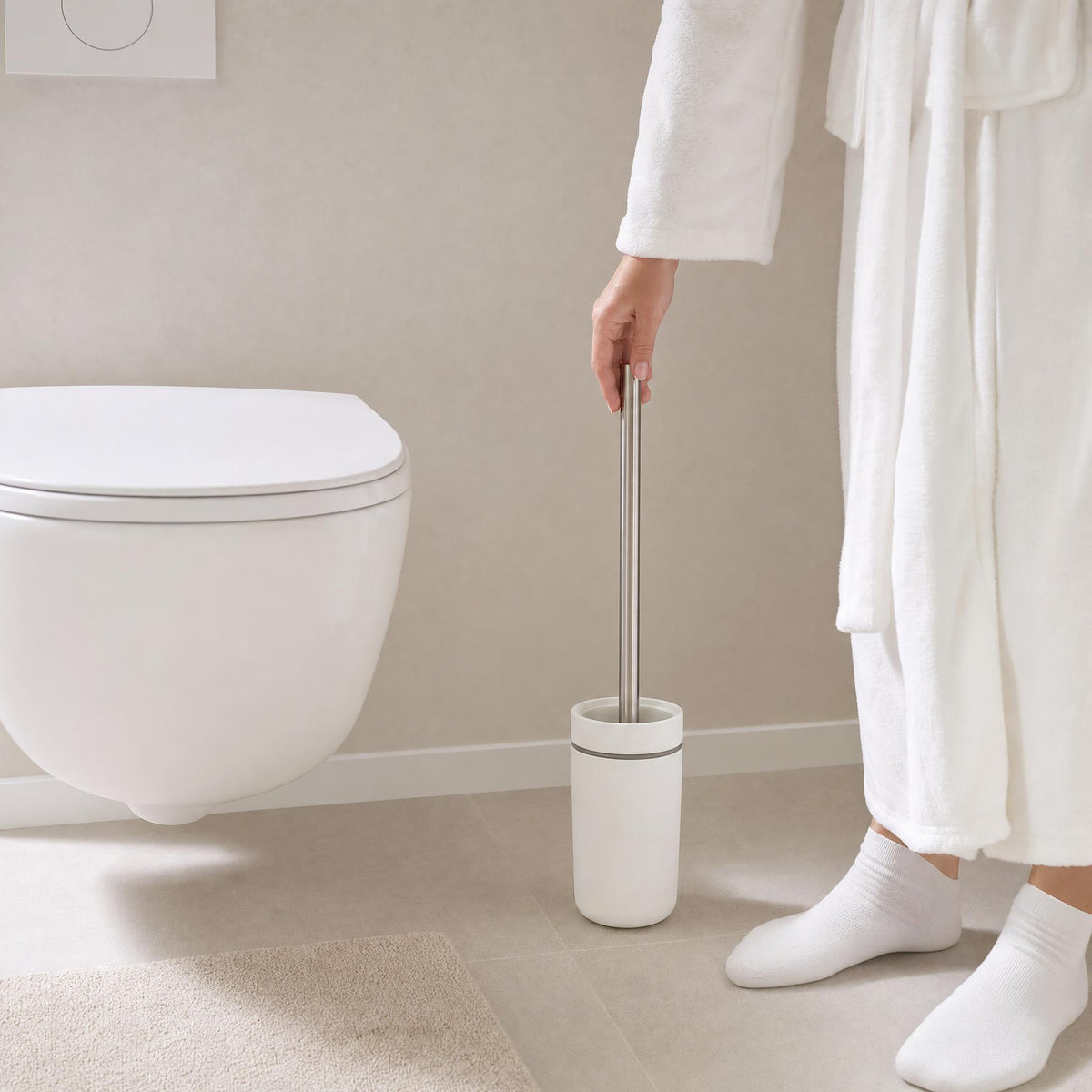 Person im Bademantel hält WC-Bürste neben modernem weißen WC.
