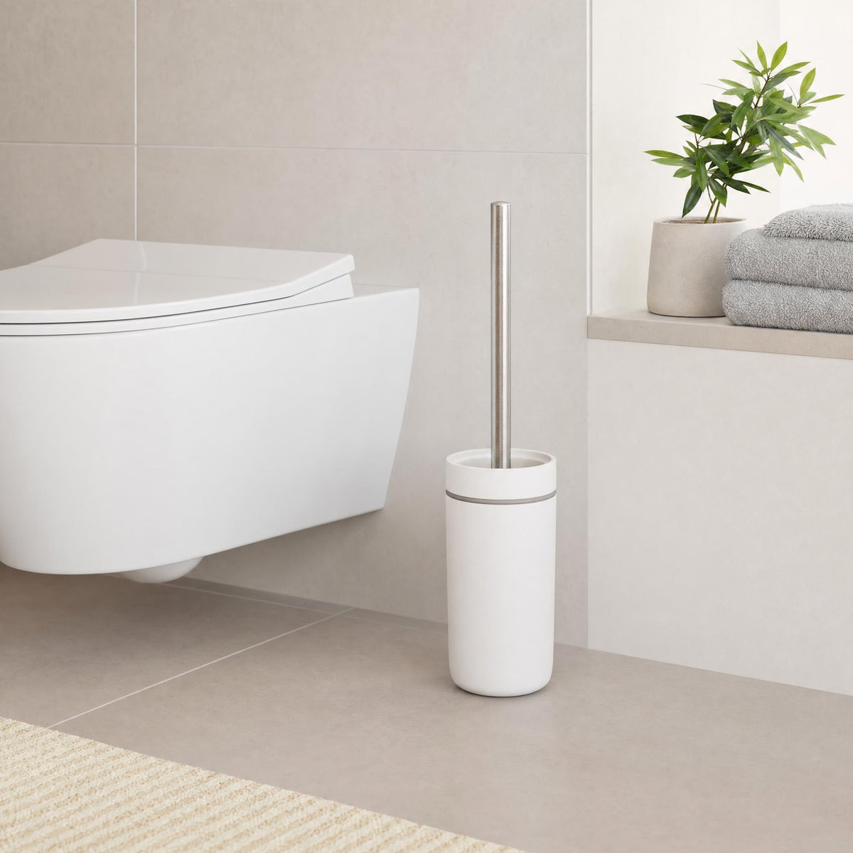 Weiße WC-Bürste neben wandhängendem WC in modernem Badezimmer.