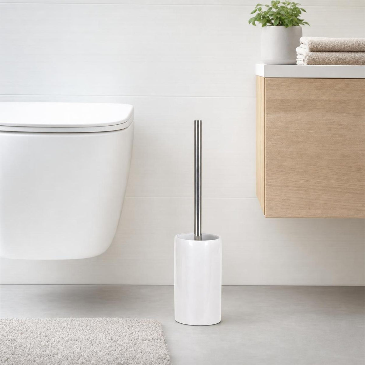 Weiße WC-Bürste mit Chromgriff steht neben Toilette und Badschrank.