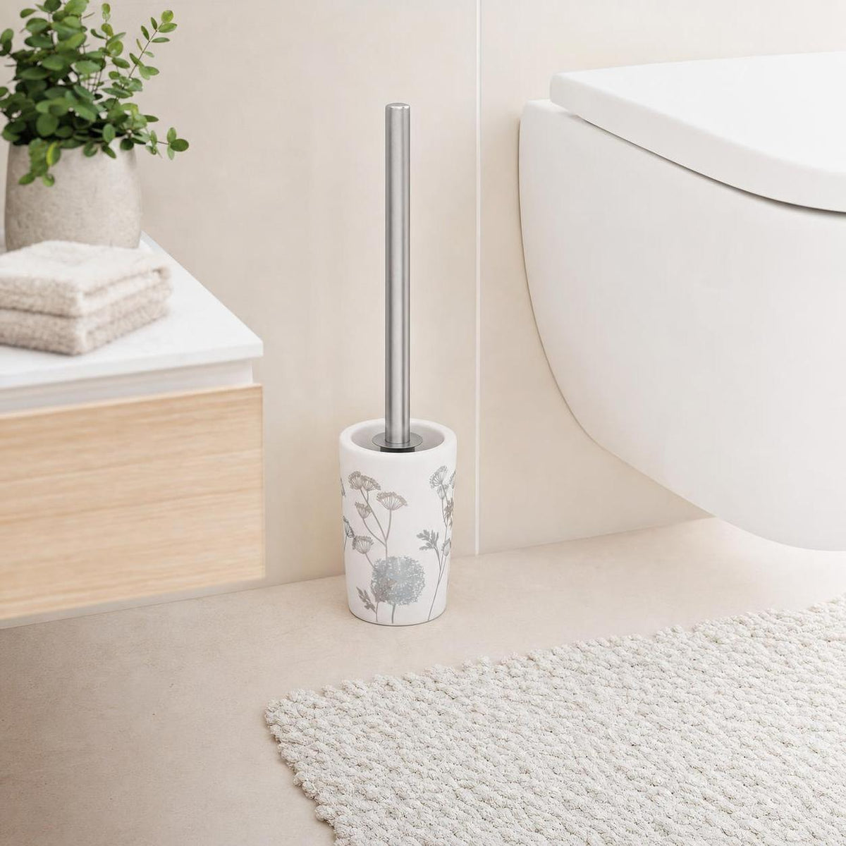Weiße WC-Bürste mit Blumenmuster steht neben der Toilette im Bad.