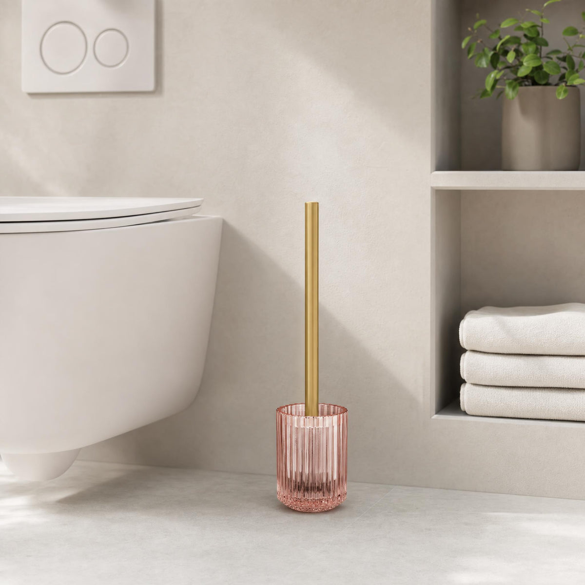 Rosa WC-Bürste mit Goldgriff in modernem Bad neben Regal und Toilette.