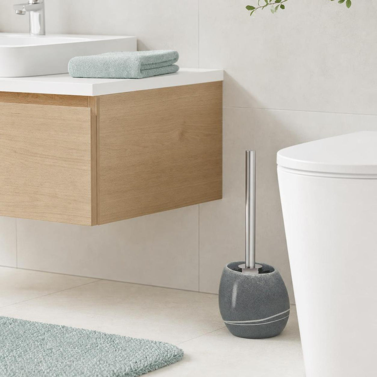 Graue WC-Bürste steht neben der Toilette in einem hellen Badezimmer.