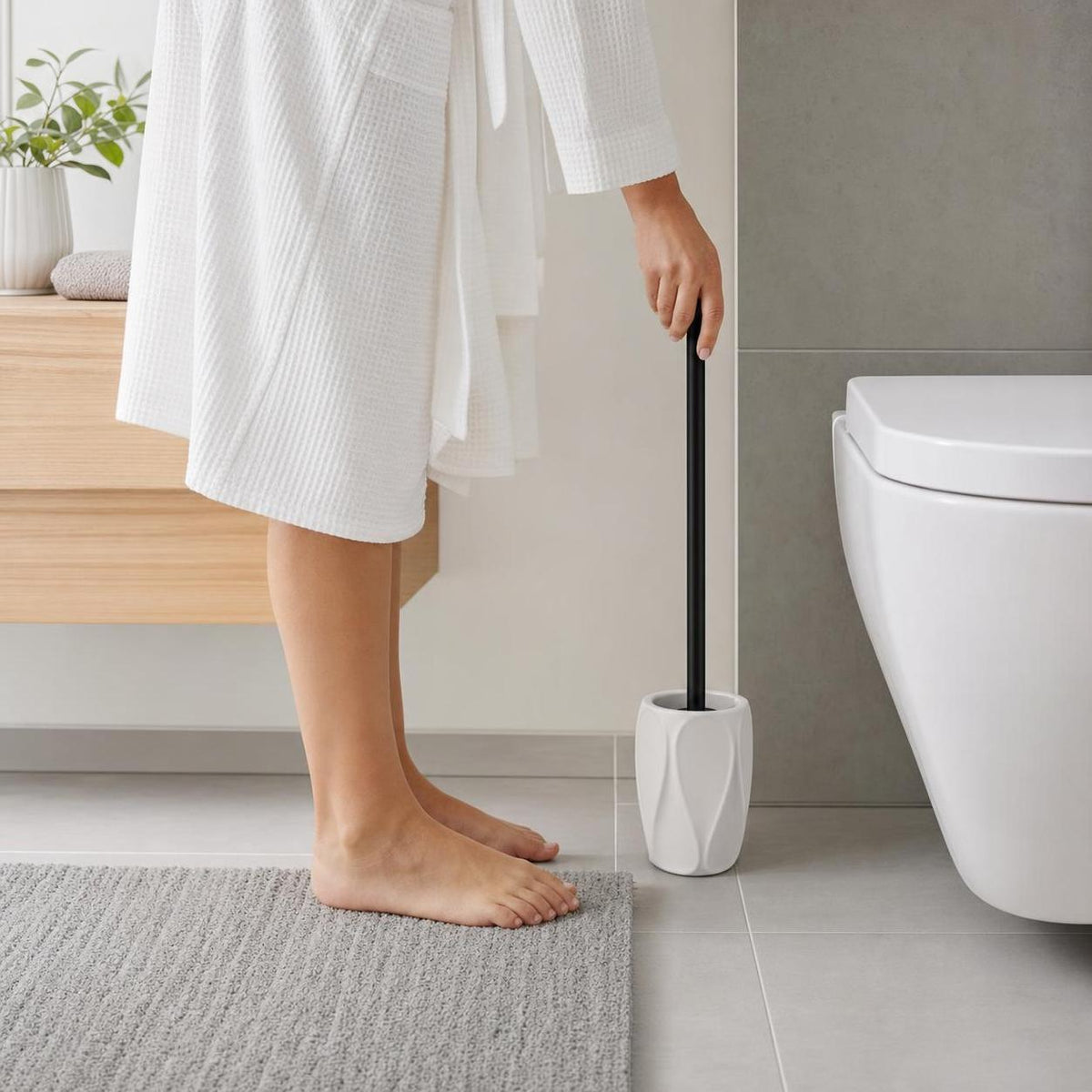Person im weißen Bademantel mit WC-Bürste neben modernem WC im Bad.