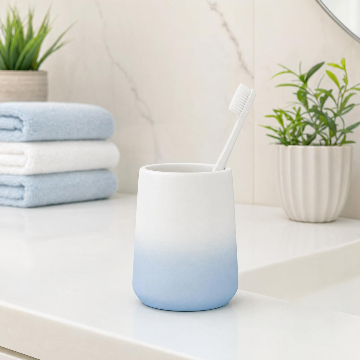 Zahnbürste im blau-weißen Becher auf Waschtisch, mit Handtüchern und Pflanzen.