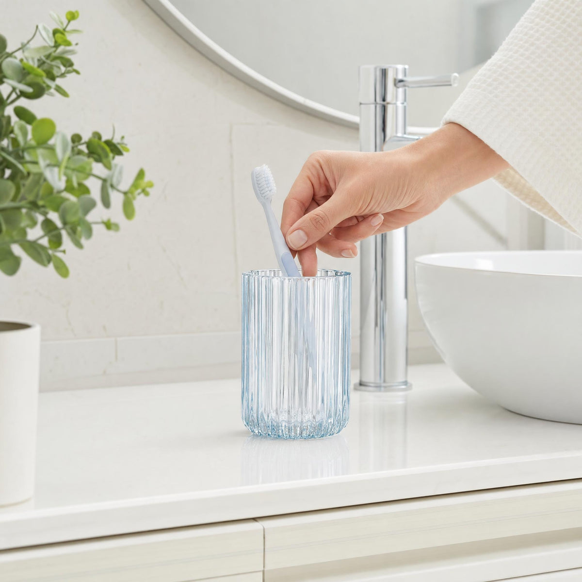 Hand legt Zahnbürste in geriffeltes Glas am modernen Waschbecken.