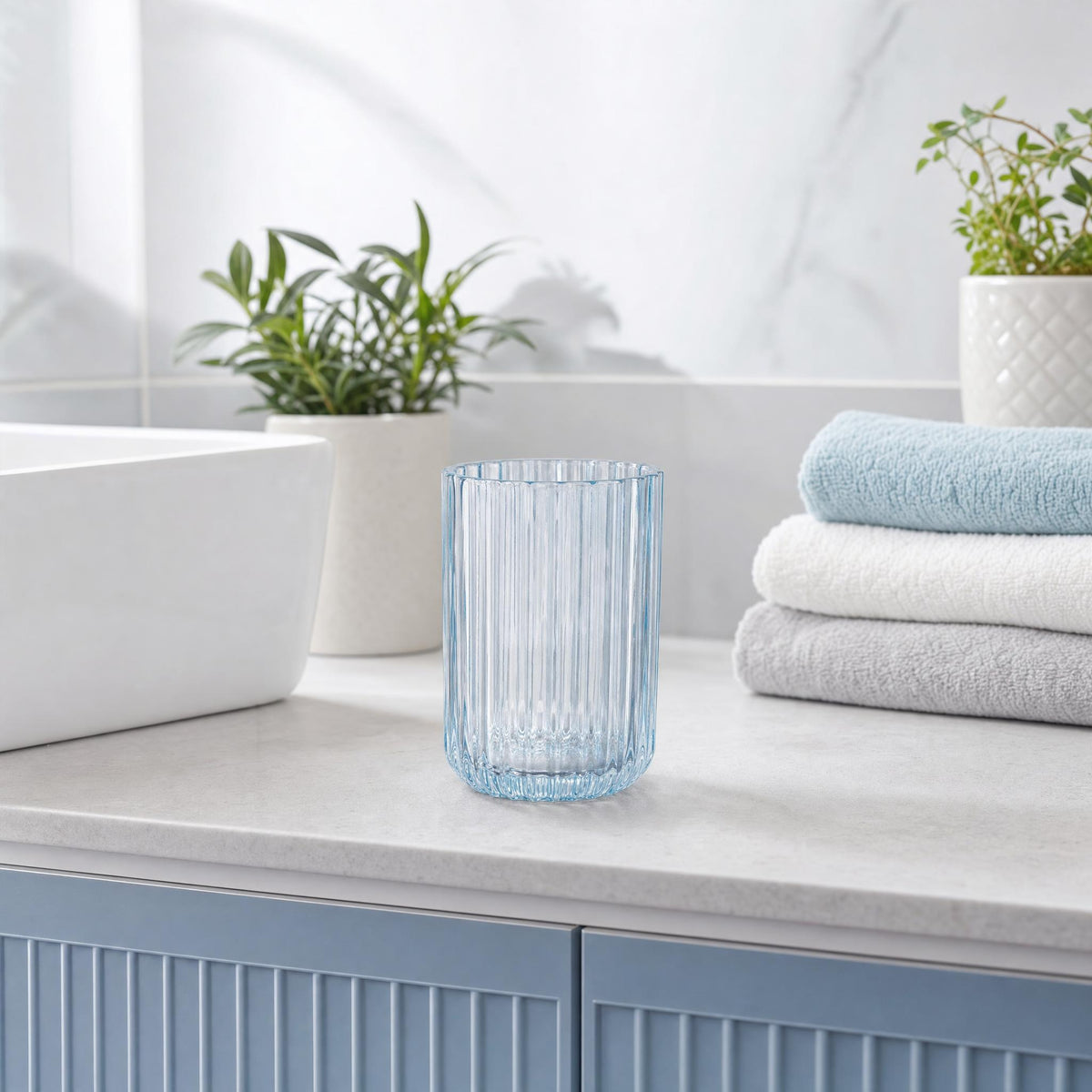 Geriffeltes blaues Glas auf Waschtisch neben Handtüchern und Pflanzen.