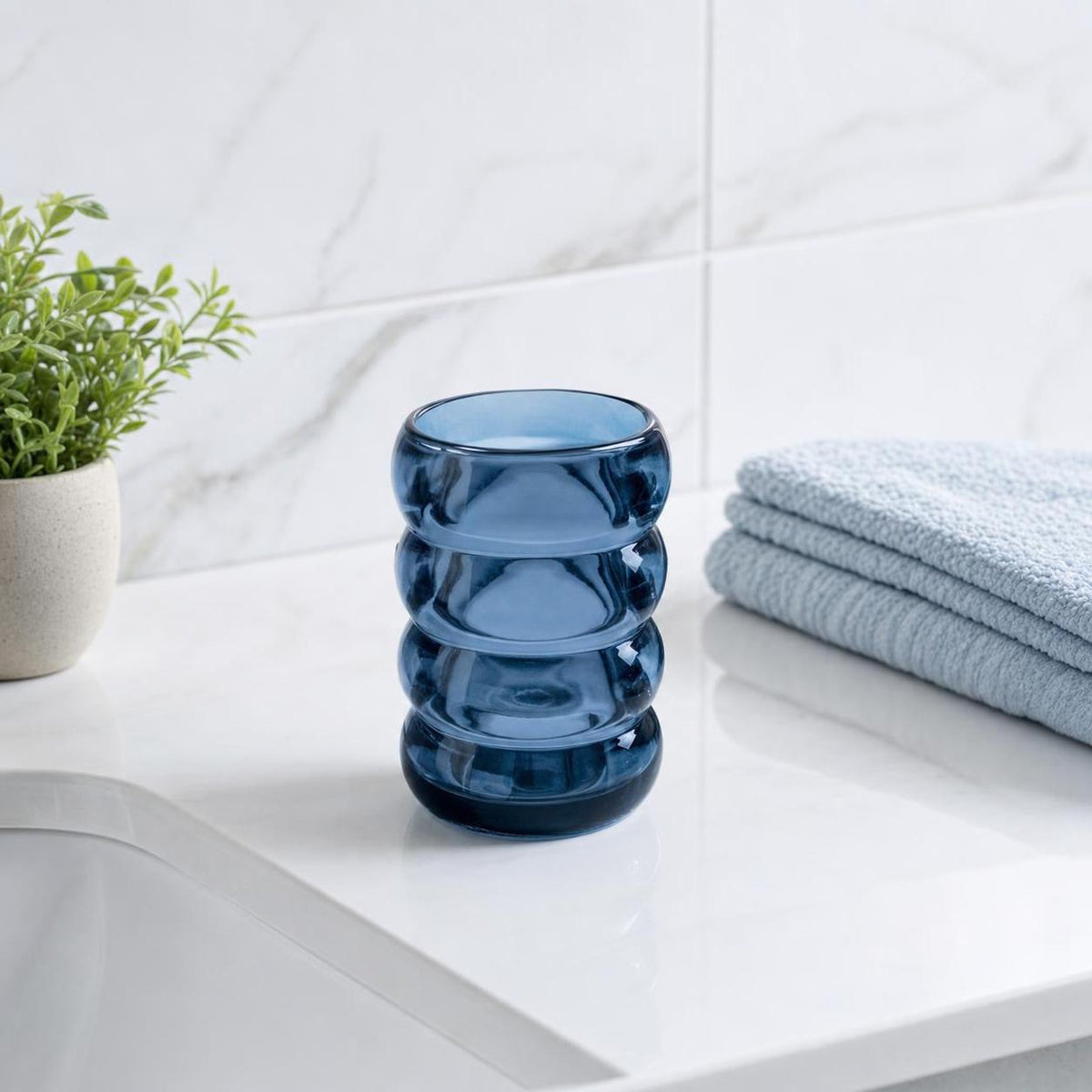 Blauer Glasbecher steht neben Handtüchern auf dem Badwaschtisch.